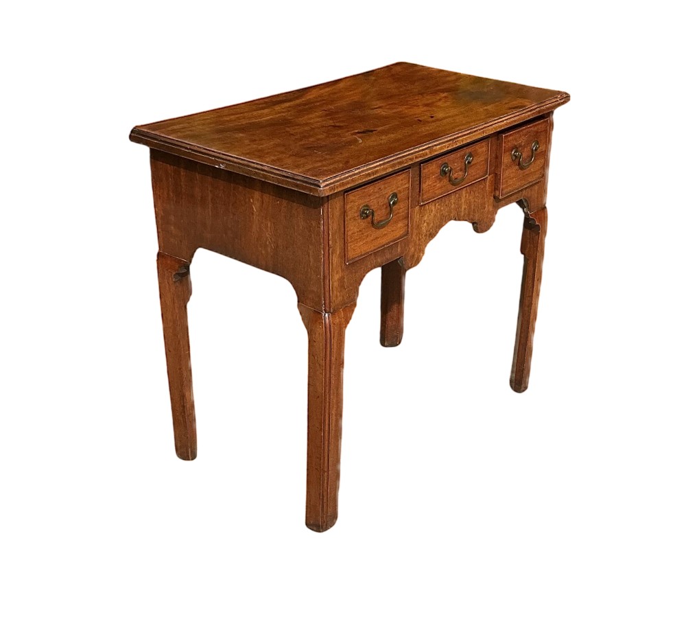 Mid-18th-century Georgian mahogany side table featuring three drawers, brass handles, a shaped apron, and four square legs.