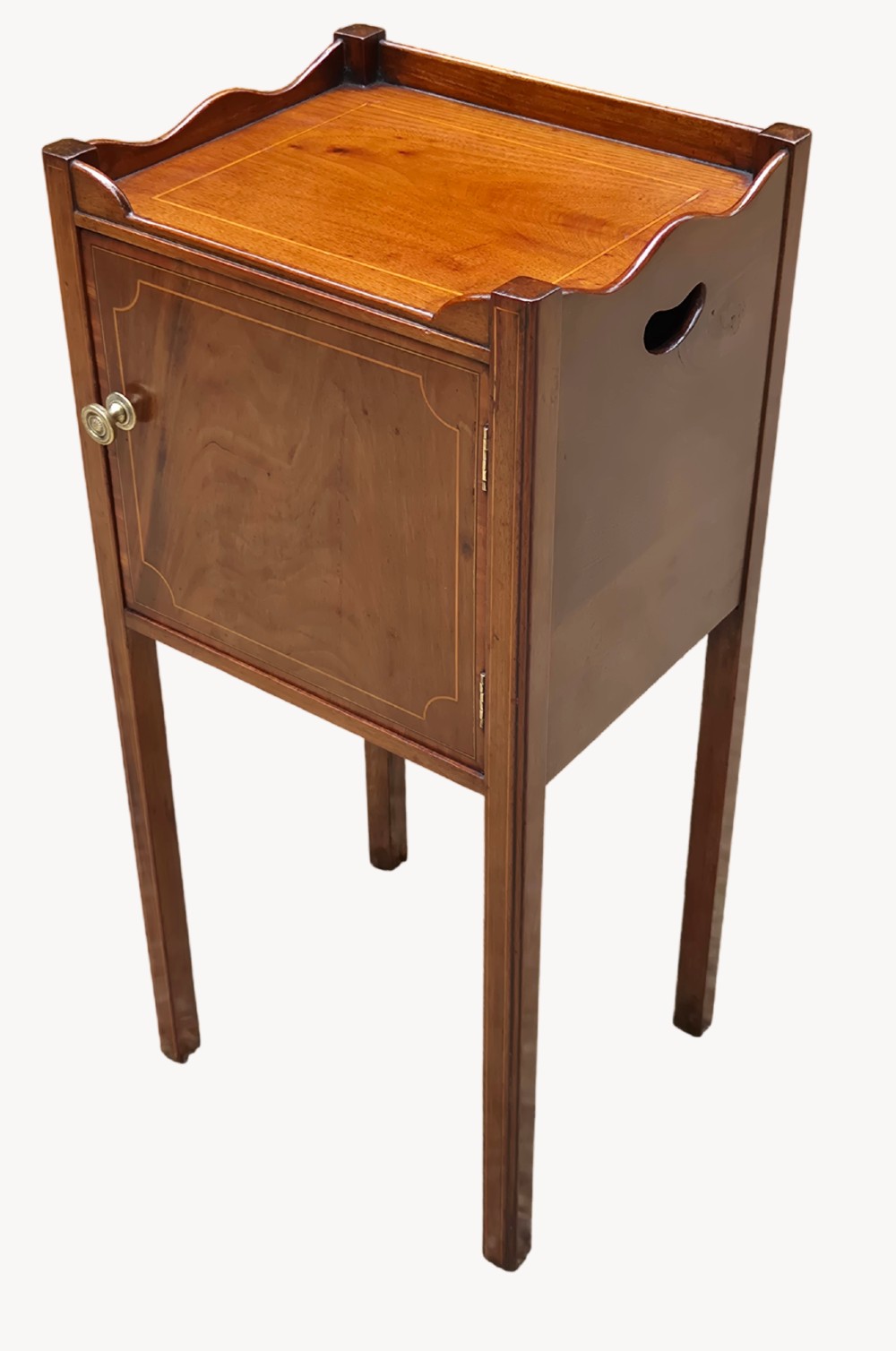 An early nineteenth-century mahogany bedside cupboard featuring a gallery tray top with handles, satinwood inlay, a single door with a brass turn handle, and square tapered legs.