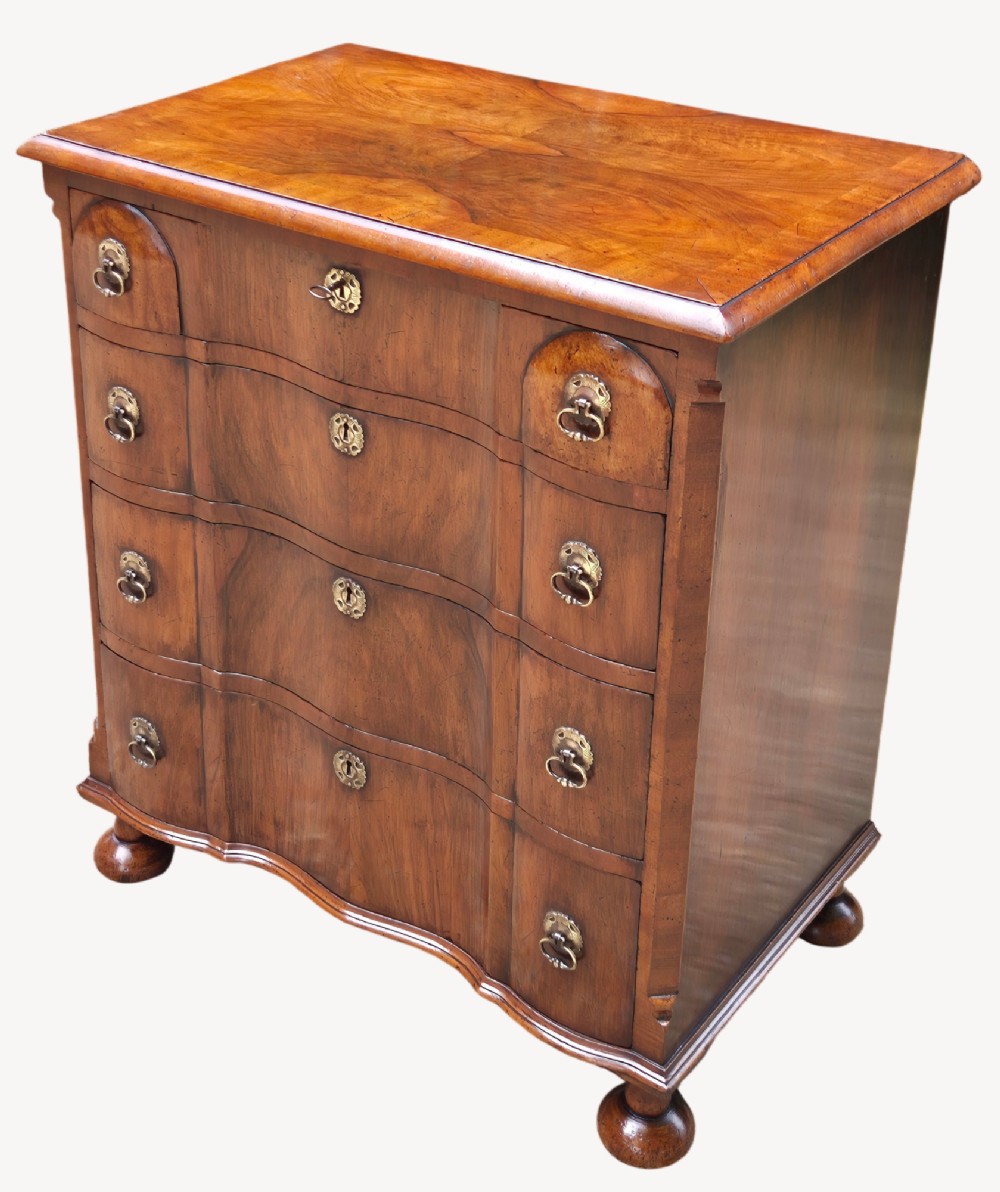 A Queen Anne style walnut chest of drawers featuring a serpentine front, brass drop handles, brass keyhole escutcheons, and bun feet.