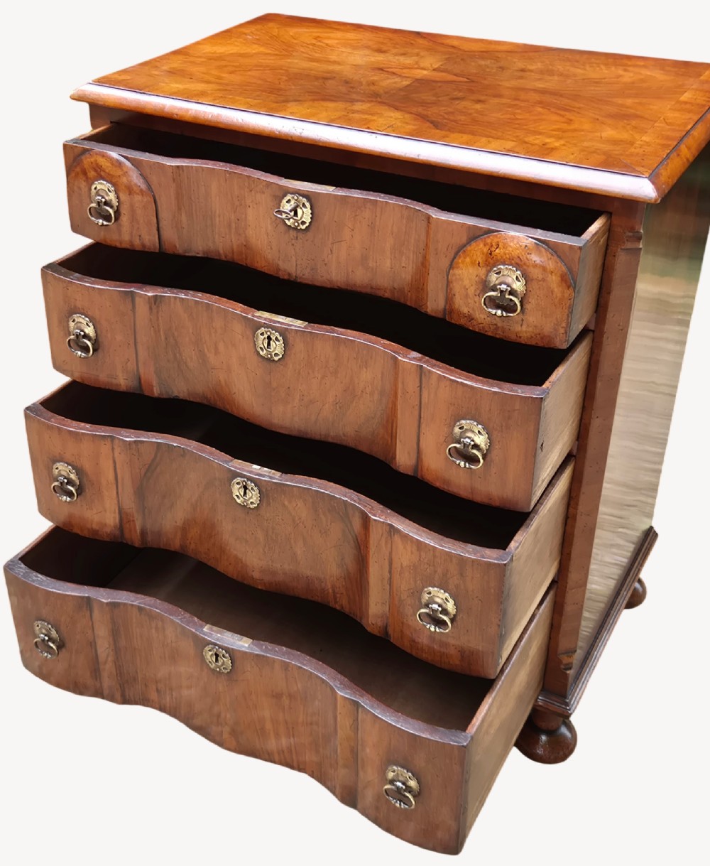 A Queen Anne style walnut chest of drawers featuring a serpentine front, brass drop handles, brass keyhole escutcheons, and bun feet. View II