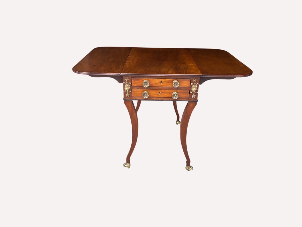 A Regency mahogany centre table featuring two drop flaps, two drawers with brass rosette handles, decorative brass appliques, and curved legs on brass castors. View II