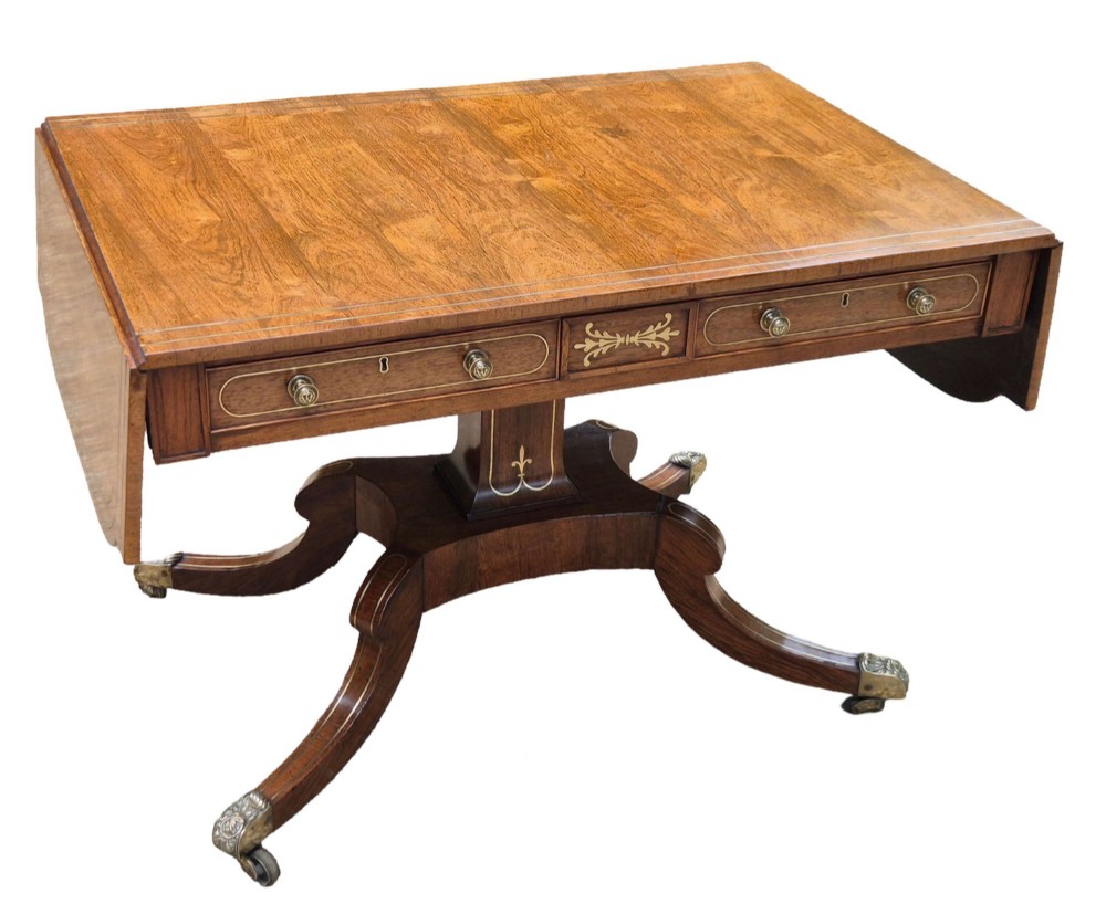 A Regency rosewood sofa table featuring hinged drop leaves, brass inlay decoration, two frieze drawers, and a quadripartite base on brass castors. View II