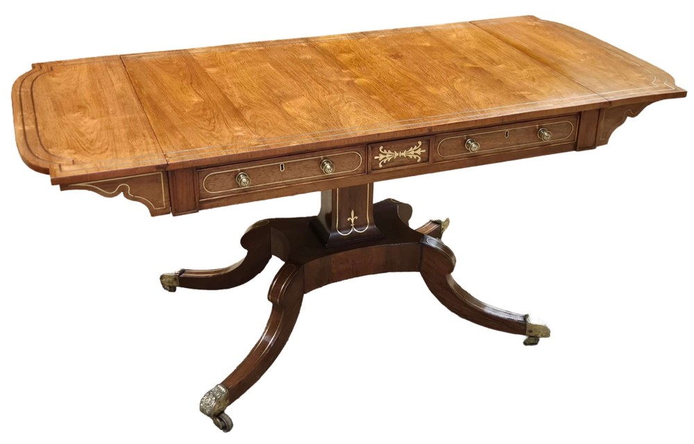 A Regency rosewood sofa table featuring hinged drop leaves, brass inlay decoration, two frieze drawers, and a quadripartite base on brass castors. View IV