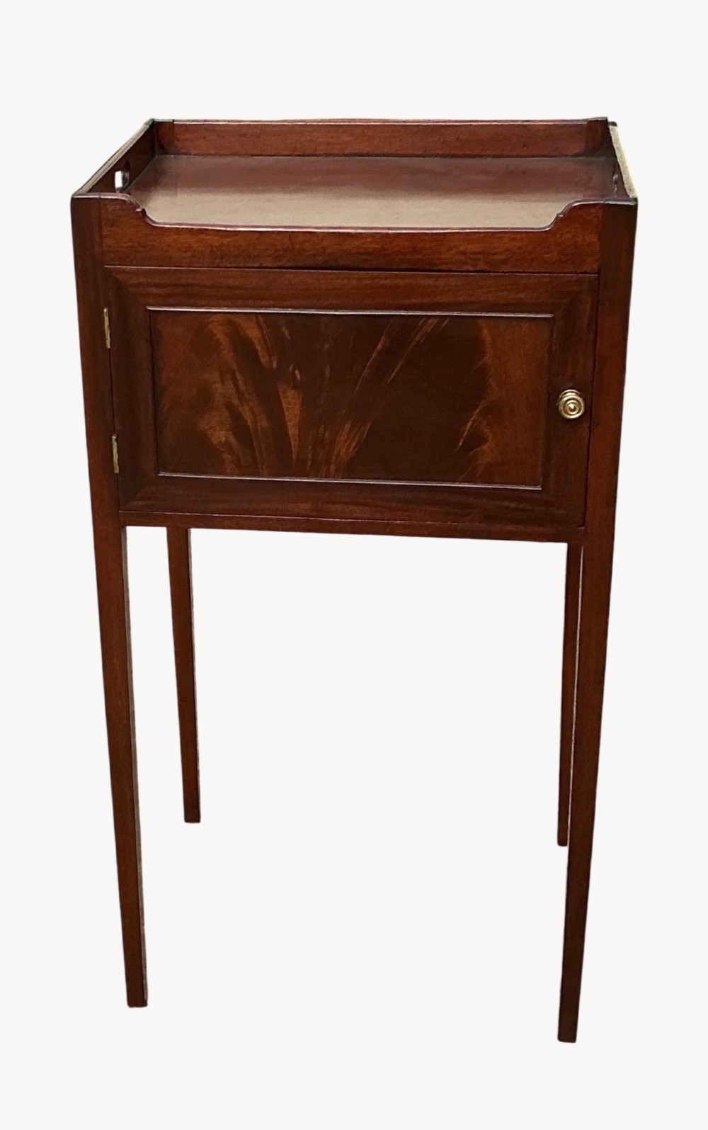 An antique Sheraton mahogany bedside cupboard featuring a tray top with cut-out handles, a single panel door with flame mahogany veneer, and square tapered legs.