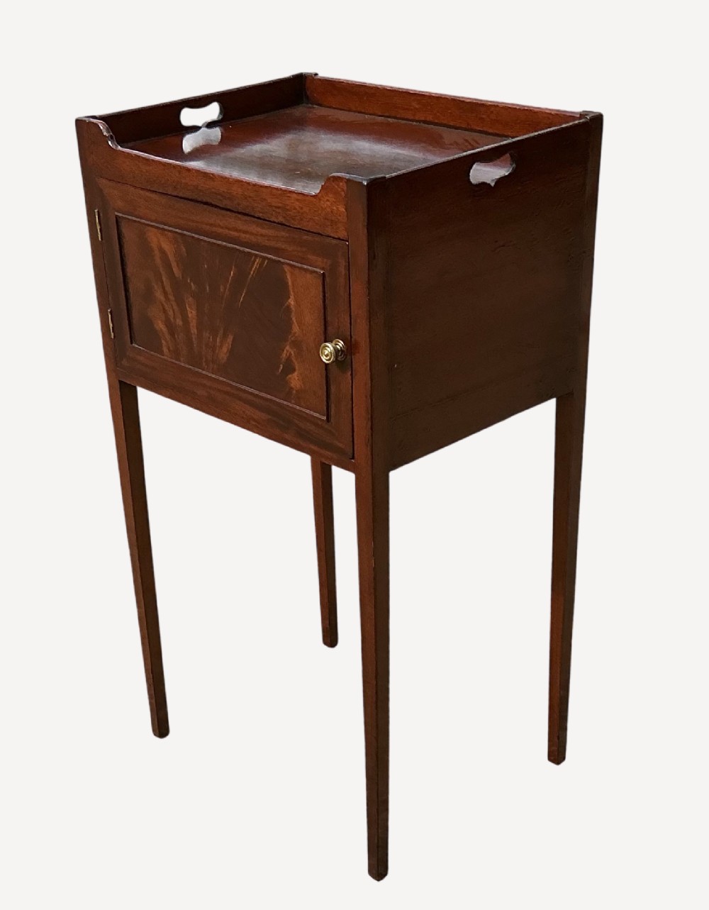 An antique Sheraton mahogany bedside cupboard featuring a tray top with cut-out handles, a single panel door with flame mahogany veneer, and square tapered legs. View II