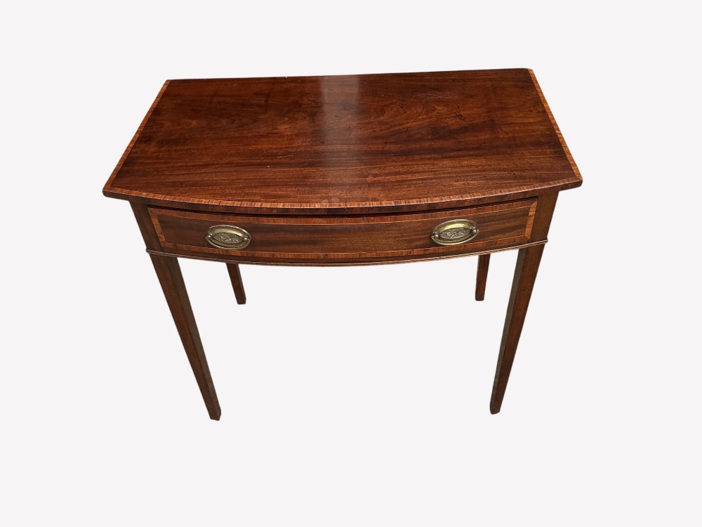 An antique mahogany Sheraton side table featuring a curved bow front, single crossbanded drawer with oval brass handles, and four square tapered legs. View III