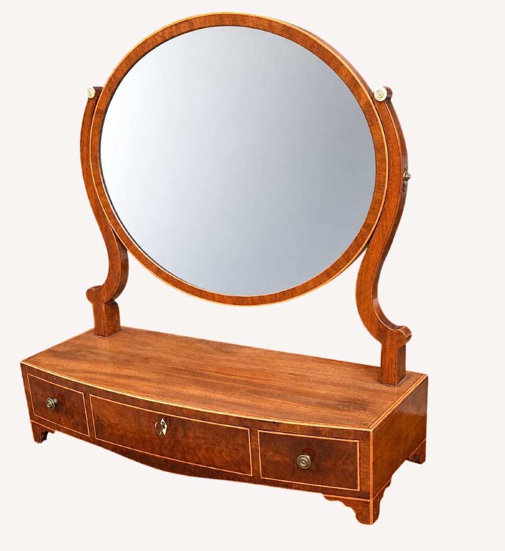 A Georgian mahogany dressing table mirror featuring an oval swing frame supported by curved uprights over a bowfront base with three drawers.