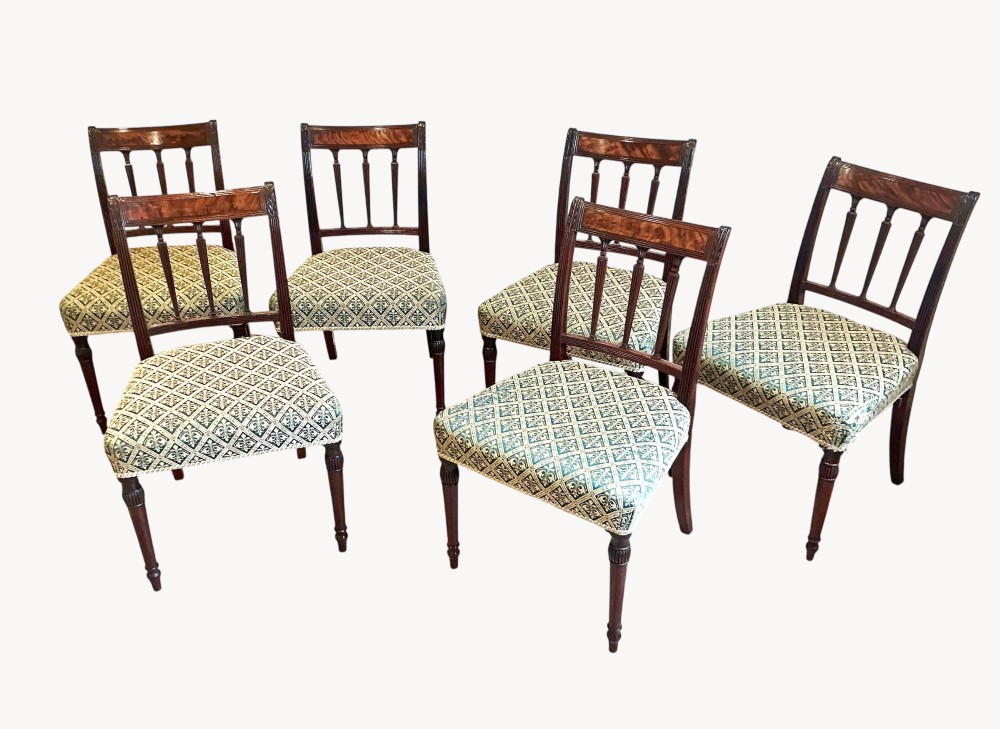 A set of six mahogany dining chairs featuring patterned fabric upholstered seats, vertical back splats, and reeded front legs.