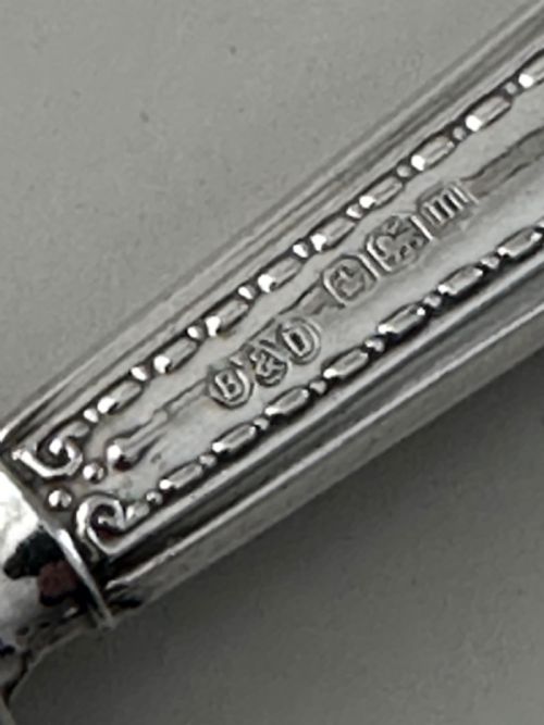 fig 1. A set of six Edwardian silver butter knives with engraved handles resting inside a dark velvet-lined presentation box.