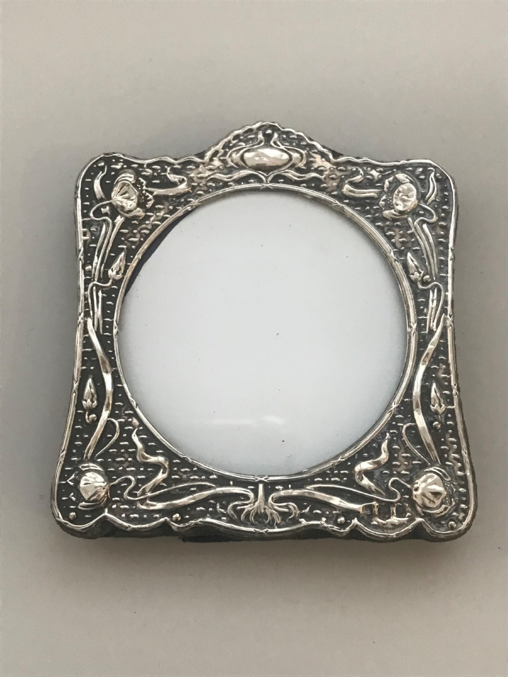 An Art Nouveau sterling silver photo frame featuring repousse floral motifs, a textured surface, and a central circular aperture.