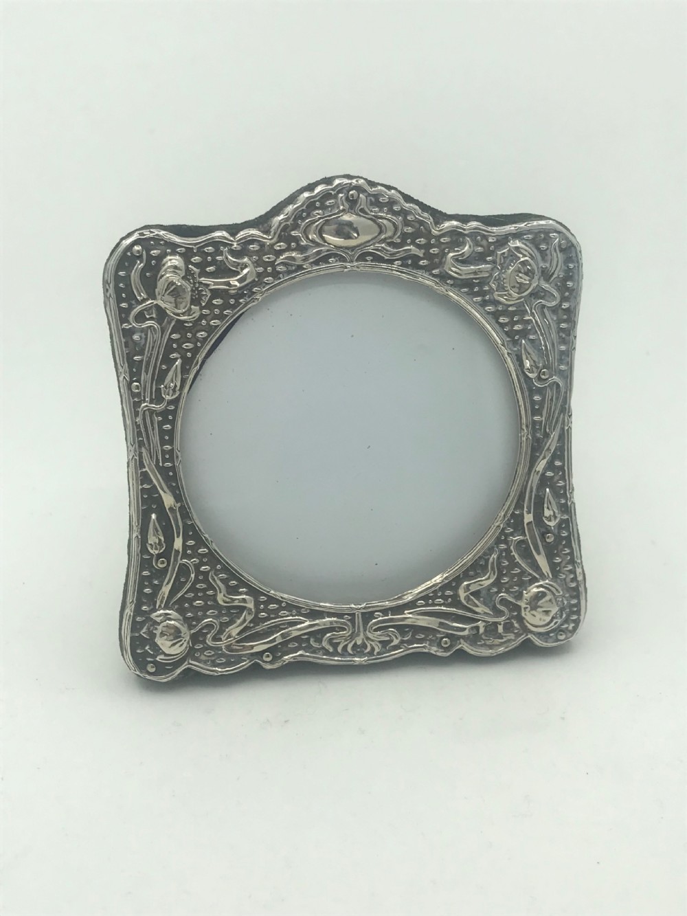 An Art Nouveau sterling silver photo frame featuring repousse floral motifs, a textured surface, and a central circular aperture. View V