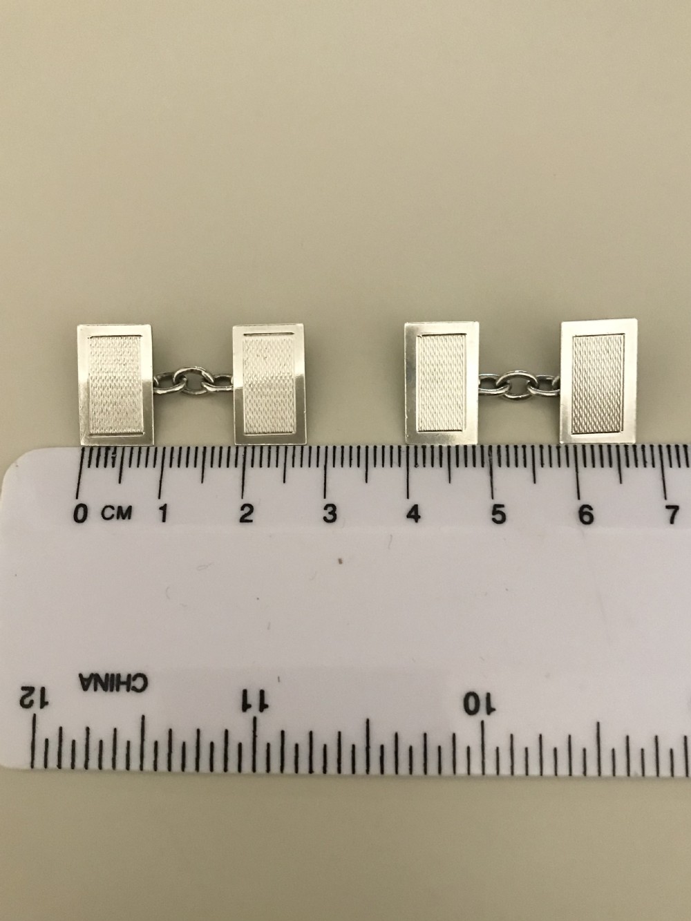 A pair of rectangular silver engine-turned cufflinks connected by chains, displayed inside an open fitted jewellers box. View II