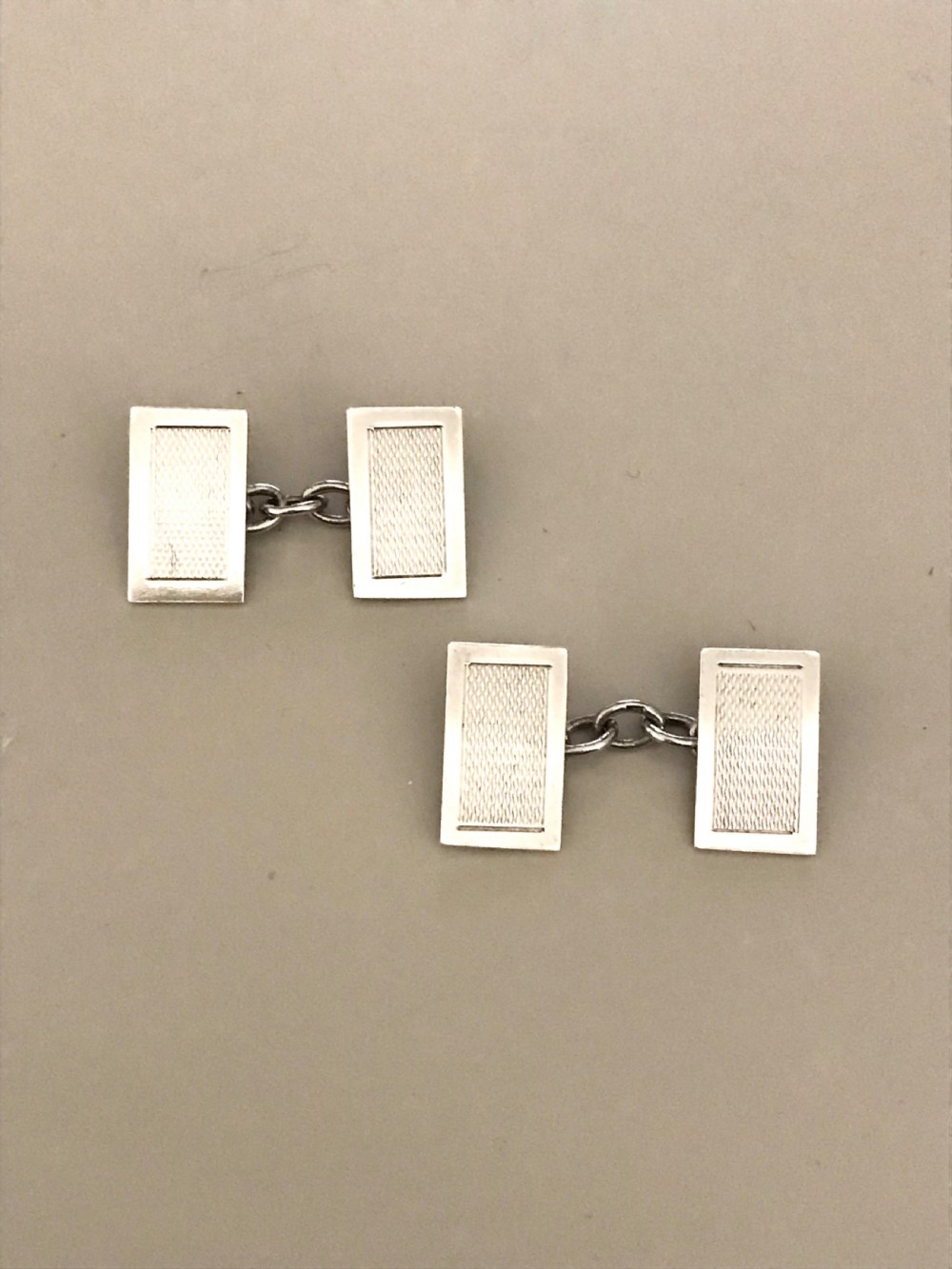 A pair of rectangular silver engine-turned cufflinks connected by chains, displayed inside an open fitted jewellers box. View IV