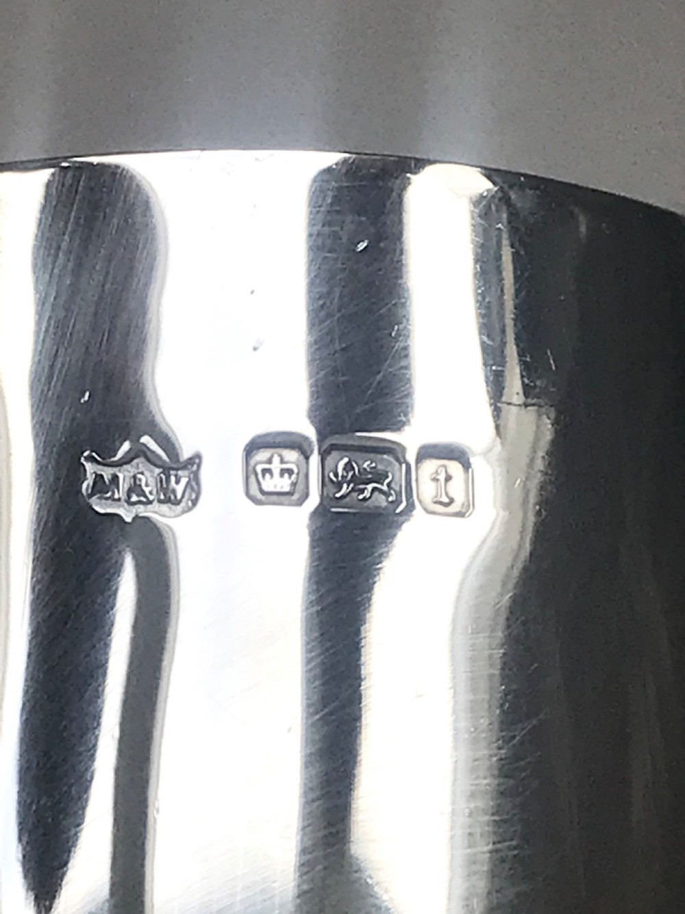 An Edwardian sterling silver christening mug featuring a tapered body, loop handle, gold gilt interior, ball feet, and visible hallmarking. View III