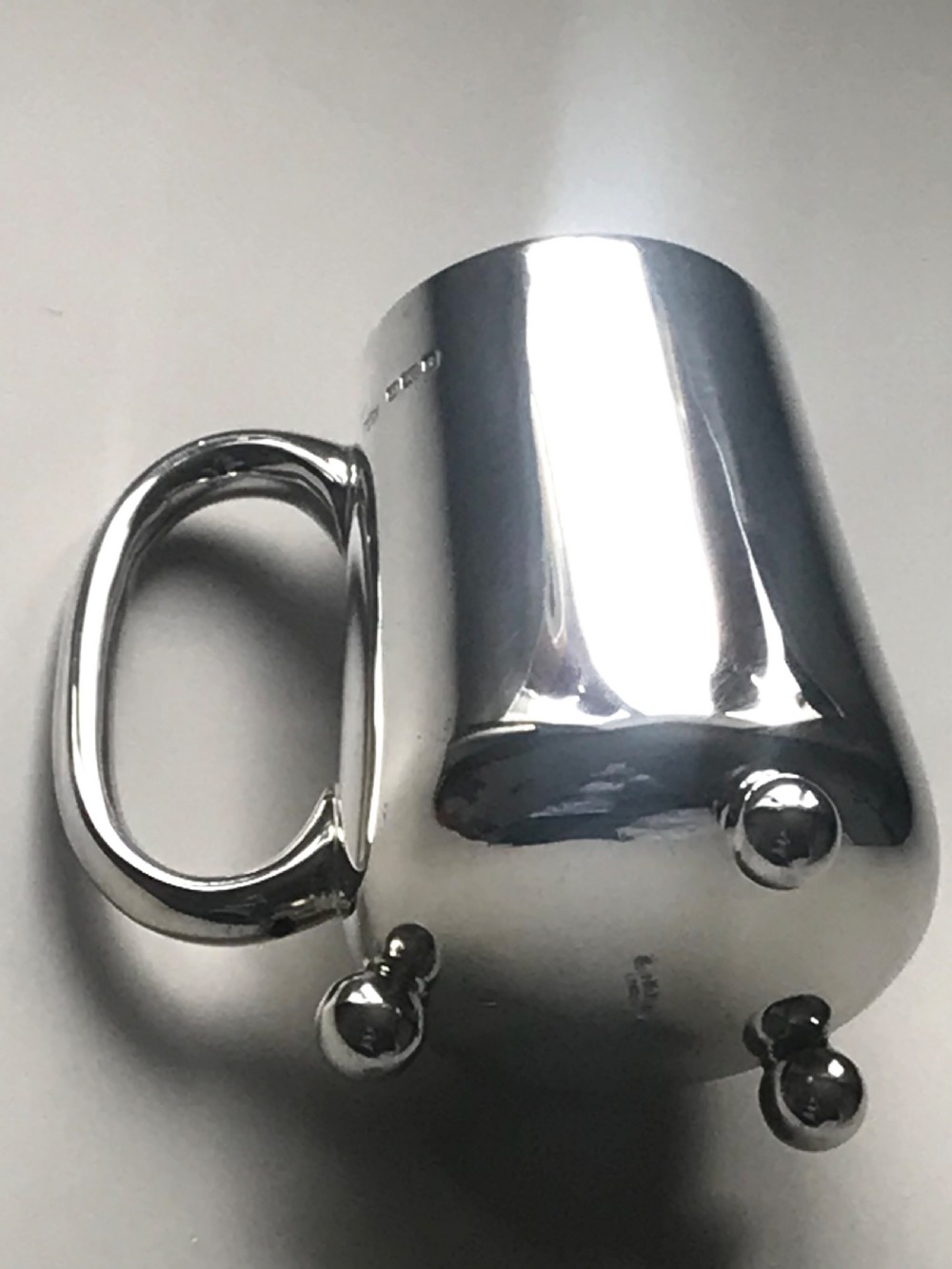 An Edwardian sterling silver christening mug featuring a tapered body, loop handle, gold gilt interior, ball feet, and visible hallmarking. View IV