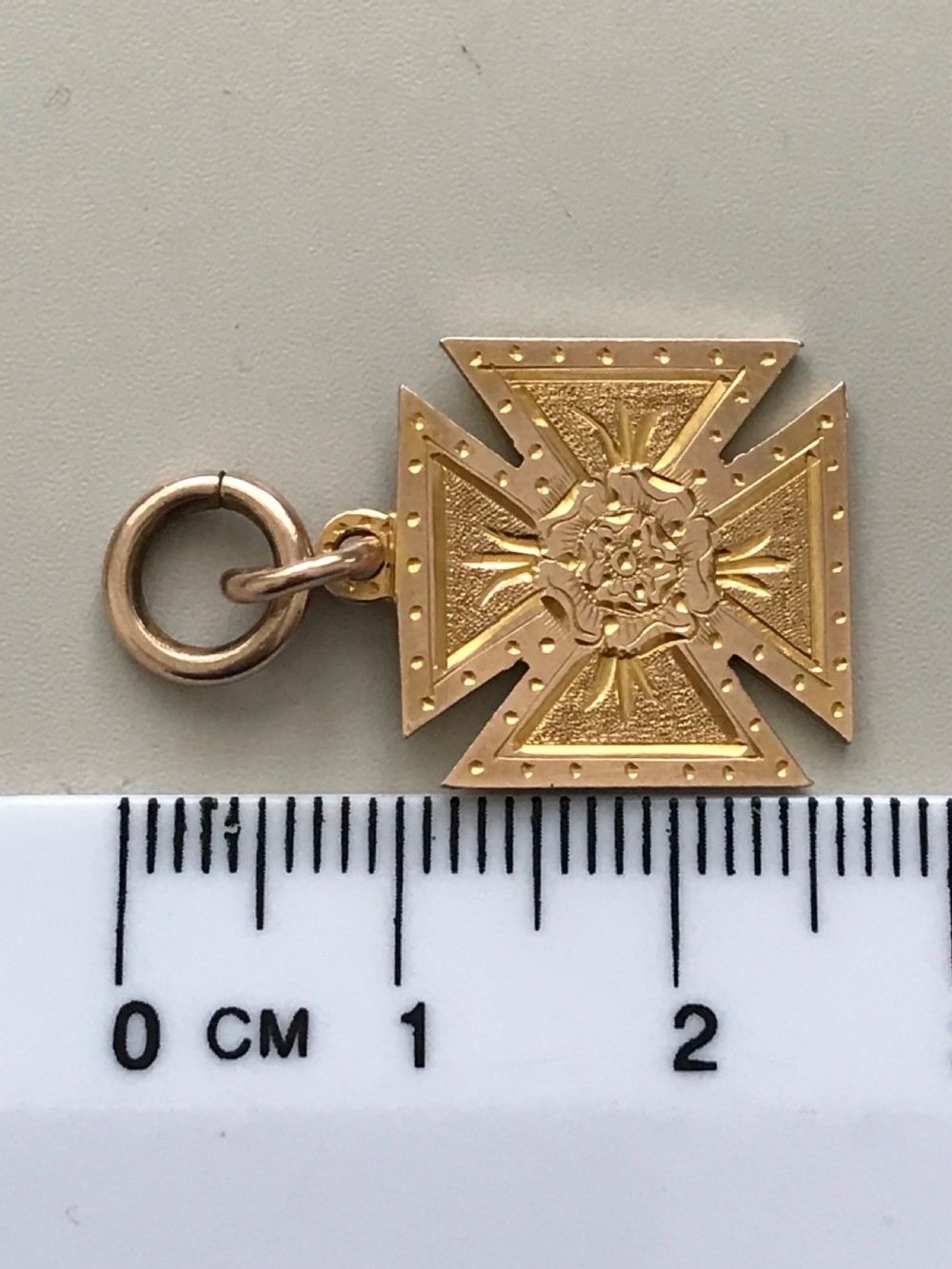 A 9ct yellow gold Maltese cross pendant featuring engraved geometric patterns, a central Tudor rose motif, and a top suspension ring. View IV
