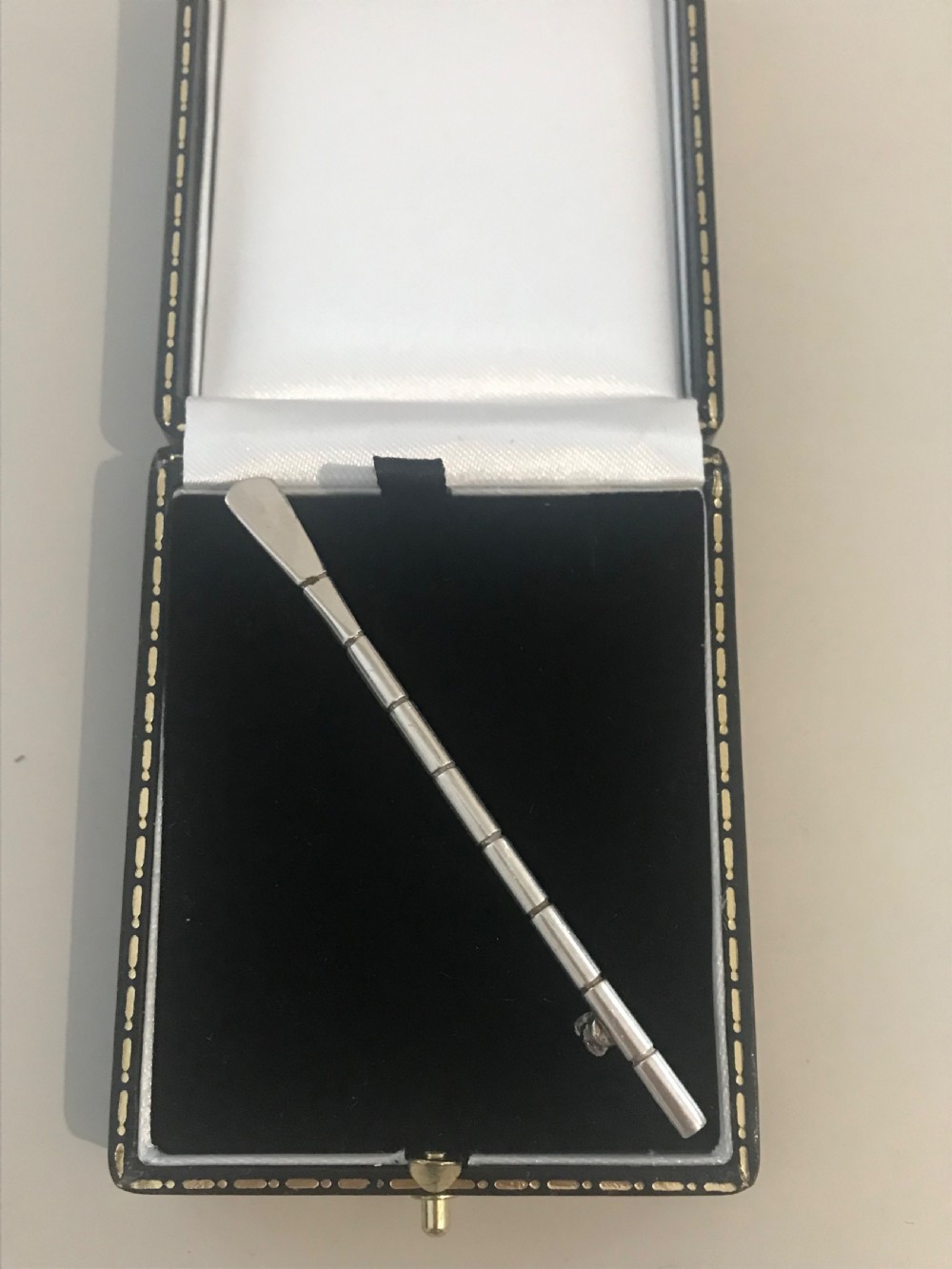 A silver brooch styled in the form of a rowing oar with a flat blade and segmented shaft.