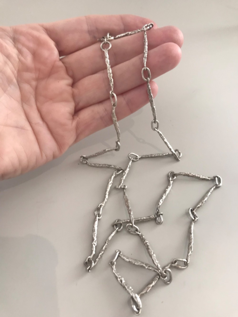 A vintage sterling silver chain necklace with elongated textured bar links presented inside a dark velvet-lined display box. View VII