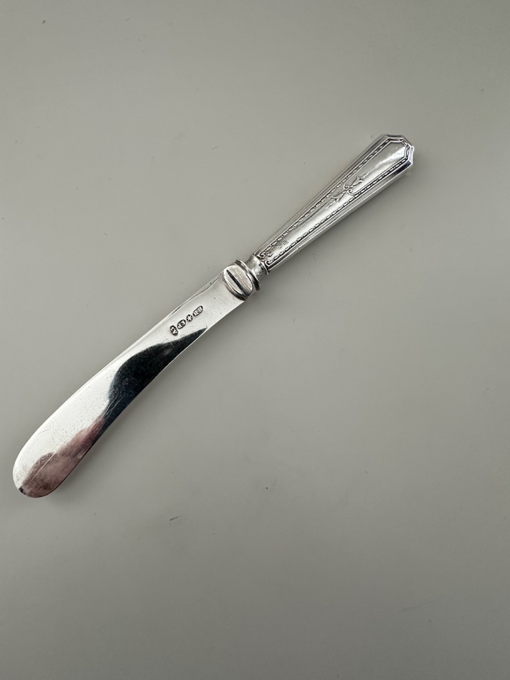 A set of six Edwardian silver butter knives with engraved handles resting inside a dark velvet-lined presentation box. View III