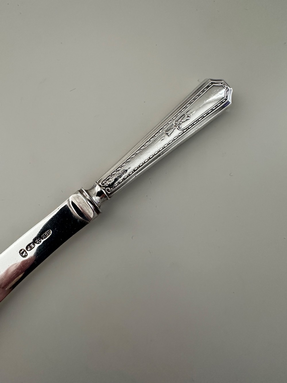 A set of six Edwardian silver butter knives with engraved handles resting inside a dark velvet-lined presentation box. View IV