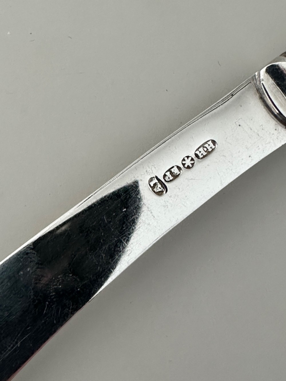 A set of six Edwardian silver butter knives with engraved handles resting inside a dark velvet-lined presentation box. View V