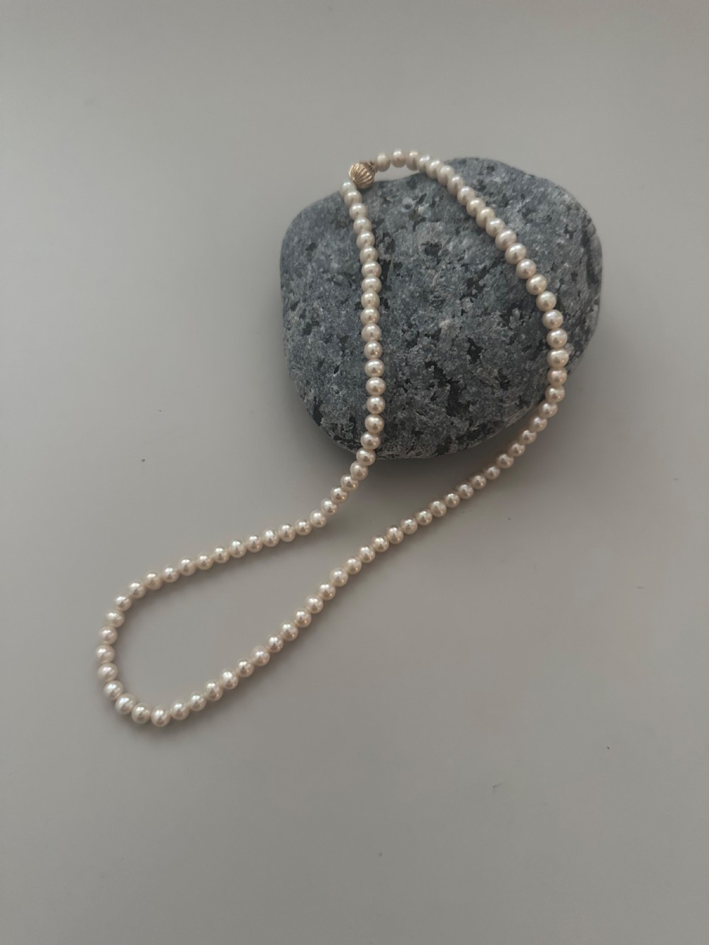 A single strand vintage cultured pearl necklace featuring uniform cream pearls and a gold shell-shaped clasp.
