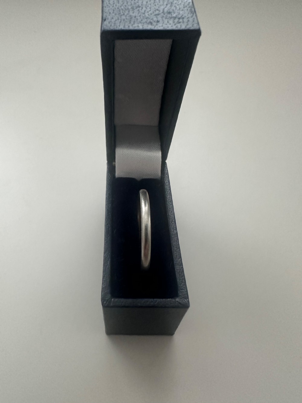 A plain platinum wedding band displayed inside an open vintage velvet-lined leather ring box. View VI