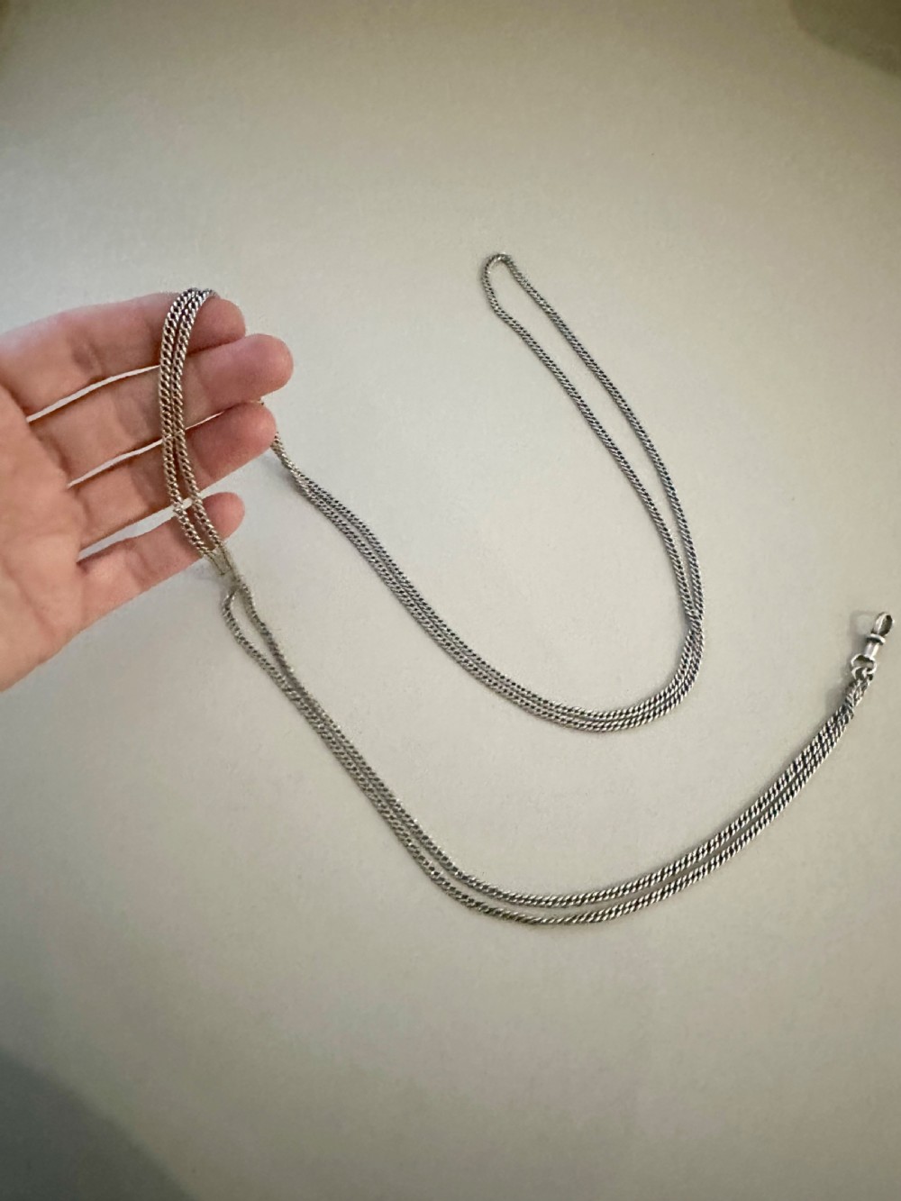 A long, finely linked Victorian sterling silver guard chain featuring an attached swivel clasp, shown coiled on a flat surface. View III