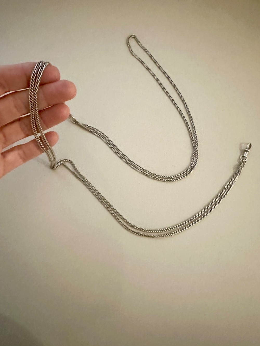 A long, finely linked Victorian sterling silver guard chain featuring an attached swivel clasp, shown coiled on a flat surface. View V