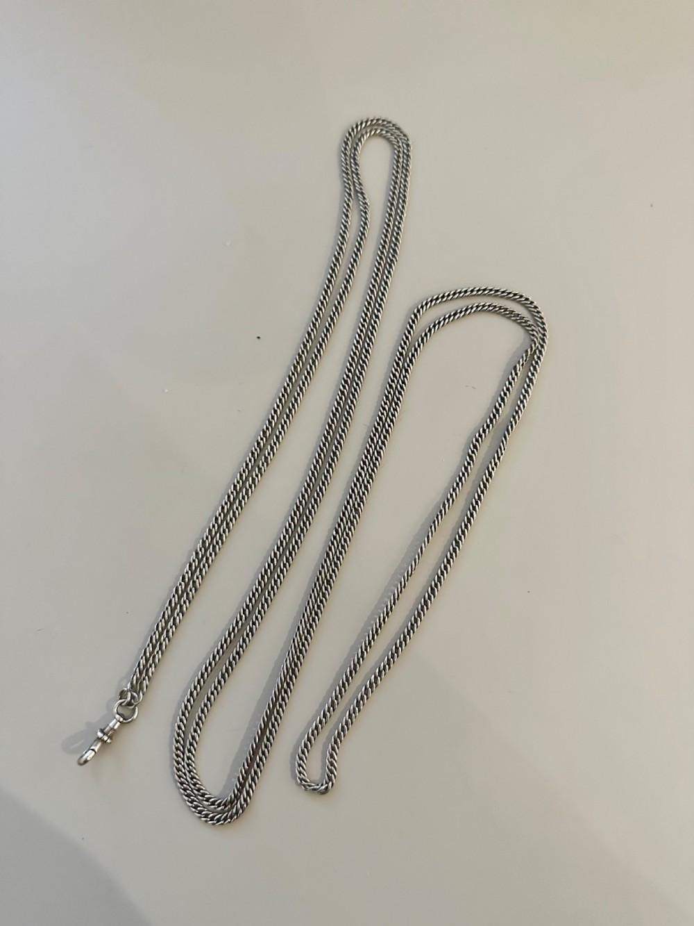 A long, finely linked Victorian sterling silver guard chain featuring an attached swivel clasp, shown coiled on a flat surface. View VI