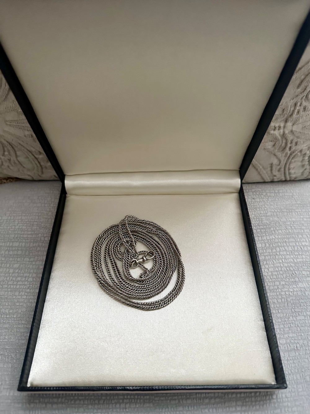 A long, finely linked Victorian sterling silver guard chain featuring an attached swivel clasp, shown coiled on a flat surface. View VII