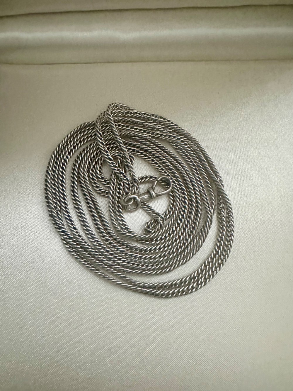 A long, finely linked Victorian sterling silver guard chain featuring an attached swivel clasp, shown coiled on a flat surface. View VIII