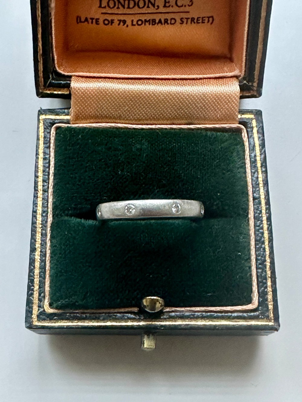 A platinum ring band inset with round diamonds sitting inside a fitted velvet presentation box.