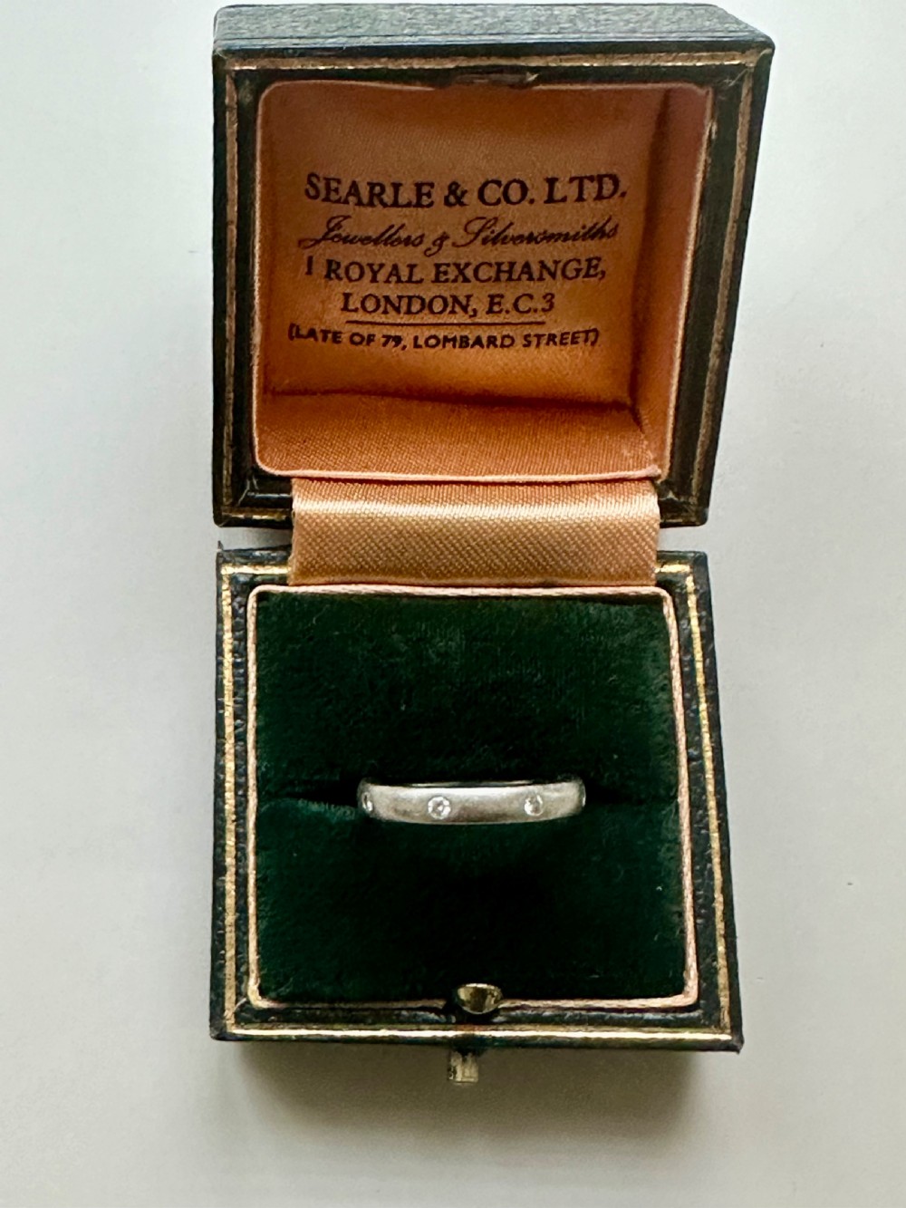A platinum ring band inset with round diamonds sitting inside a fitted velvet presentation box. View IX
