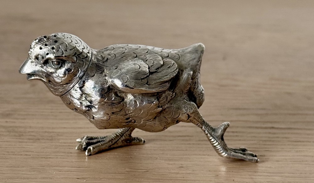 A cast silver pepper pot sculpted in the realistic shape of a chick with detailed feather engraving and a pierced head. View X