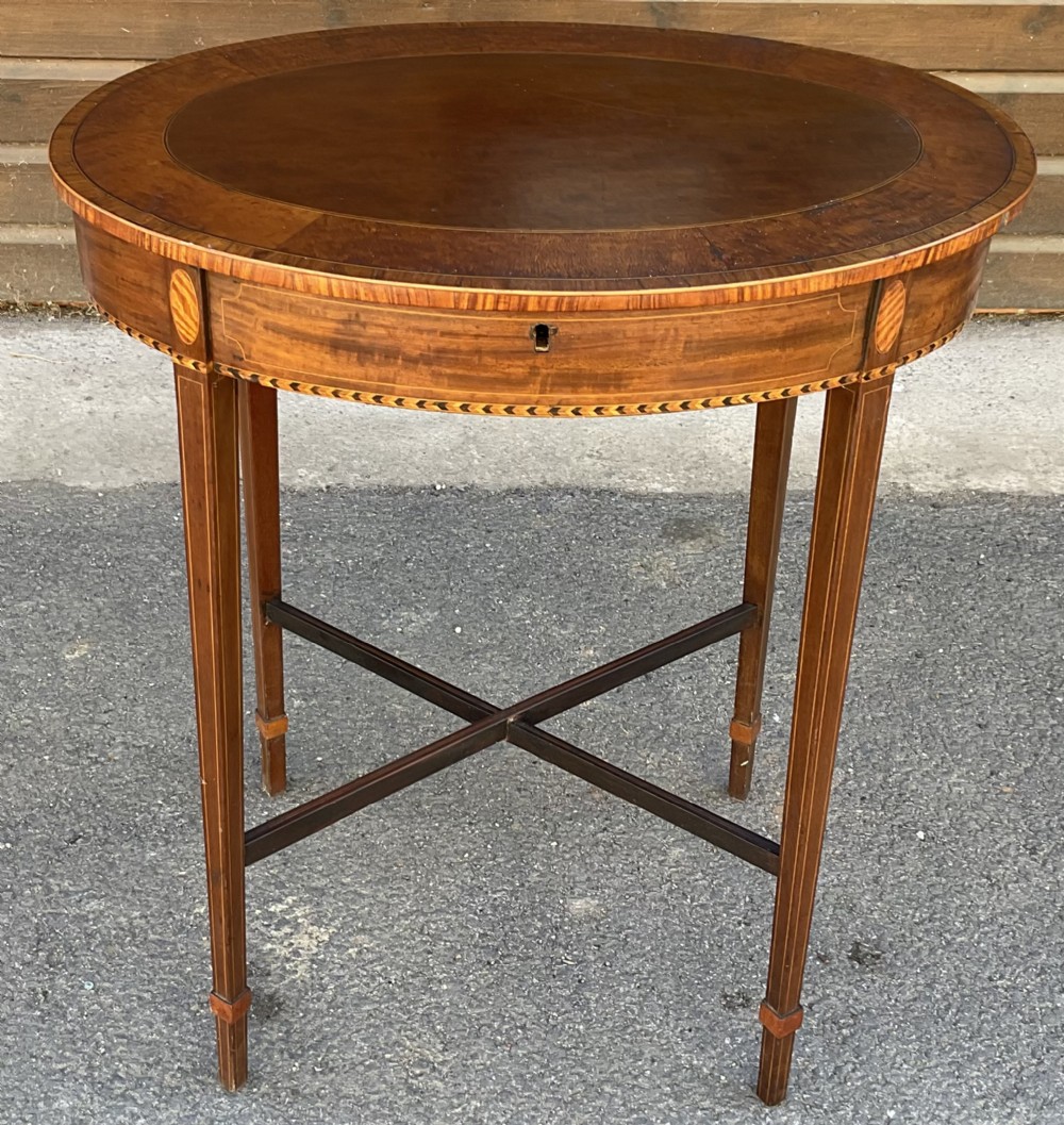 An Edwardian oval mahogany occasional table featuring satinwood inlay, tapered legs, a low cross-stretcher, and an inlaid apron.
