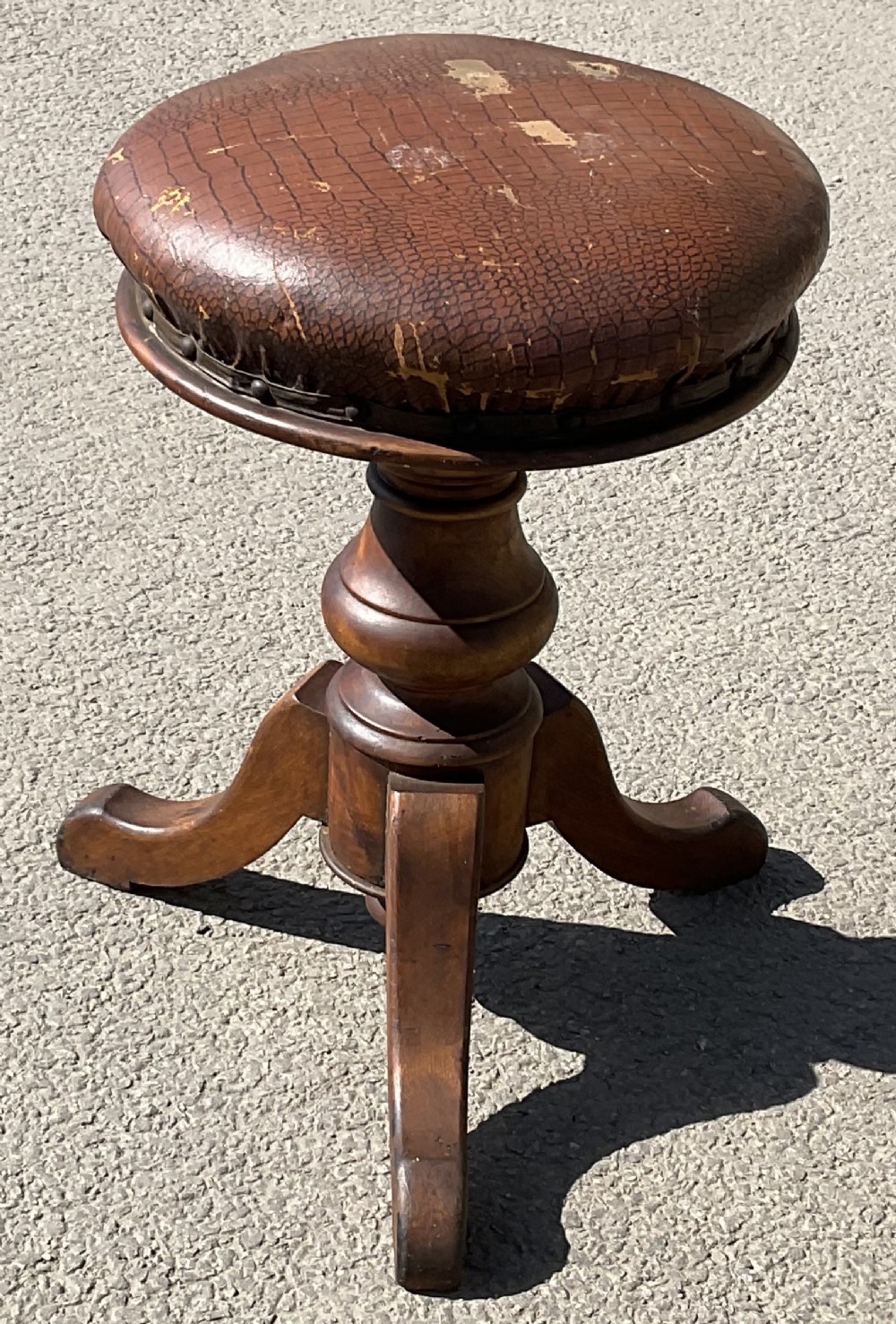 Victorian walnut piano stool with a circular textured brown leather upholstered top, turned pedestal stem, and tripod legs.