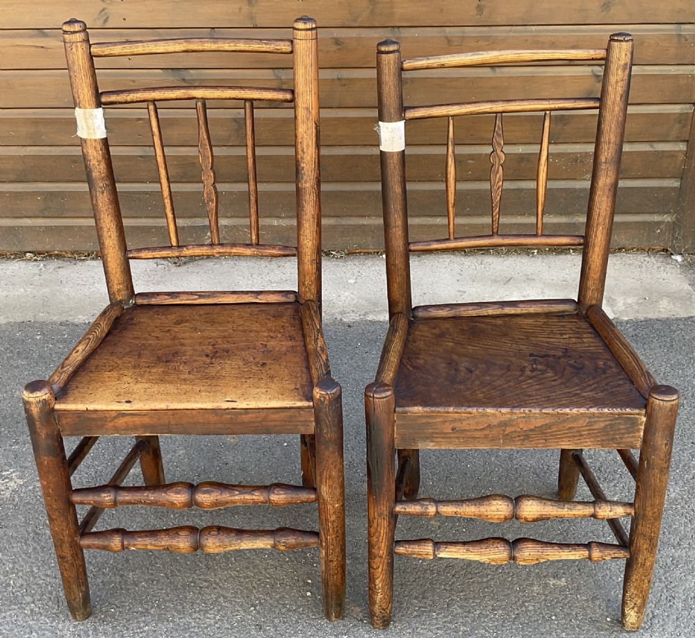 A pair of antique Victorian country chairs featuring solid elm seats, vertical spindle backs, and turned front stretchers.