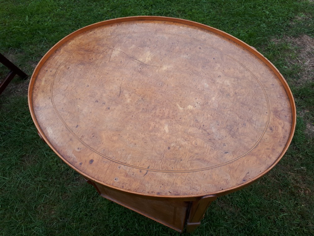 An oval golden brown burr walnut tea table featuring four extendable fold-out tray leaves supported by metal rods and standing on square tapered legs. View II