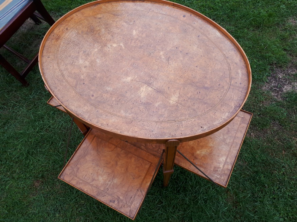 An oval golden brown burr walnut tea table featuring four extendable fold-out tray leaves supported by metal rods and standing on square tapered legs. View III
