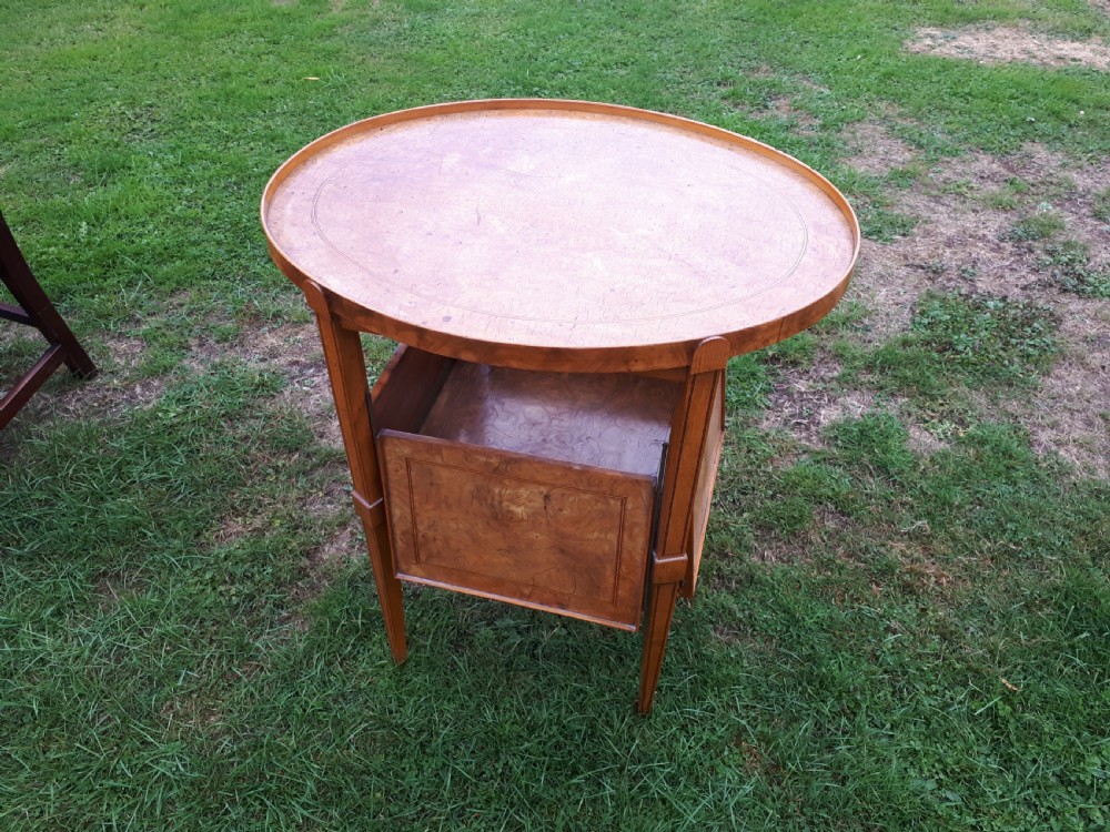 An oval golden brown burr walnut tea table featuring four extendable fold-out tray leaves supported by metal rods and standing on square tapered legs. View IV