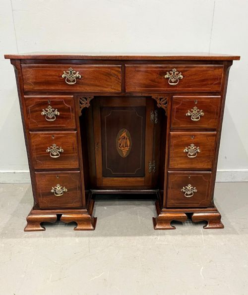 fig 1. A George III mahogany kneehole desk with multiple drawers, a recessed central inlaid door, brass handles, and bracket feet.