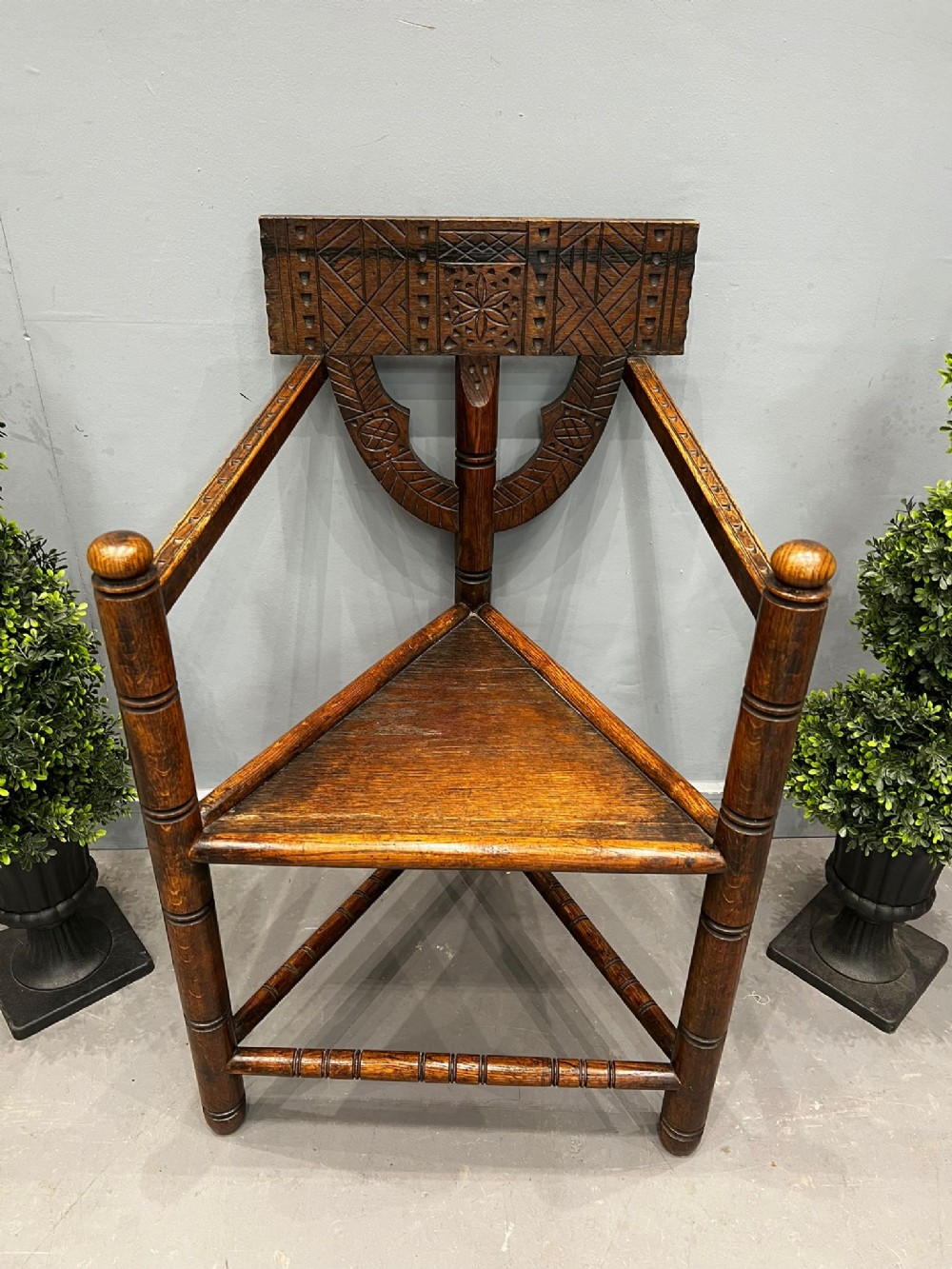 A 19th-century dark oak turner chair featuring a triangular wooden seat, turned spindles, and a carved geometric back panel with a central rosette motif.