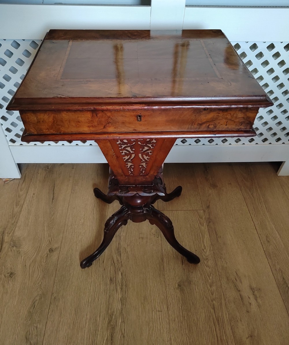A Victorian wooden trumpet sewing table with an inlaid top, fretwork column, and carved tripod base.