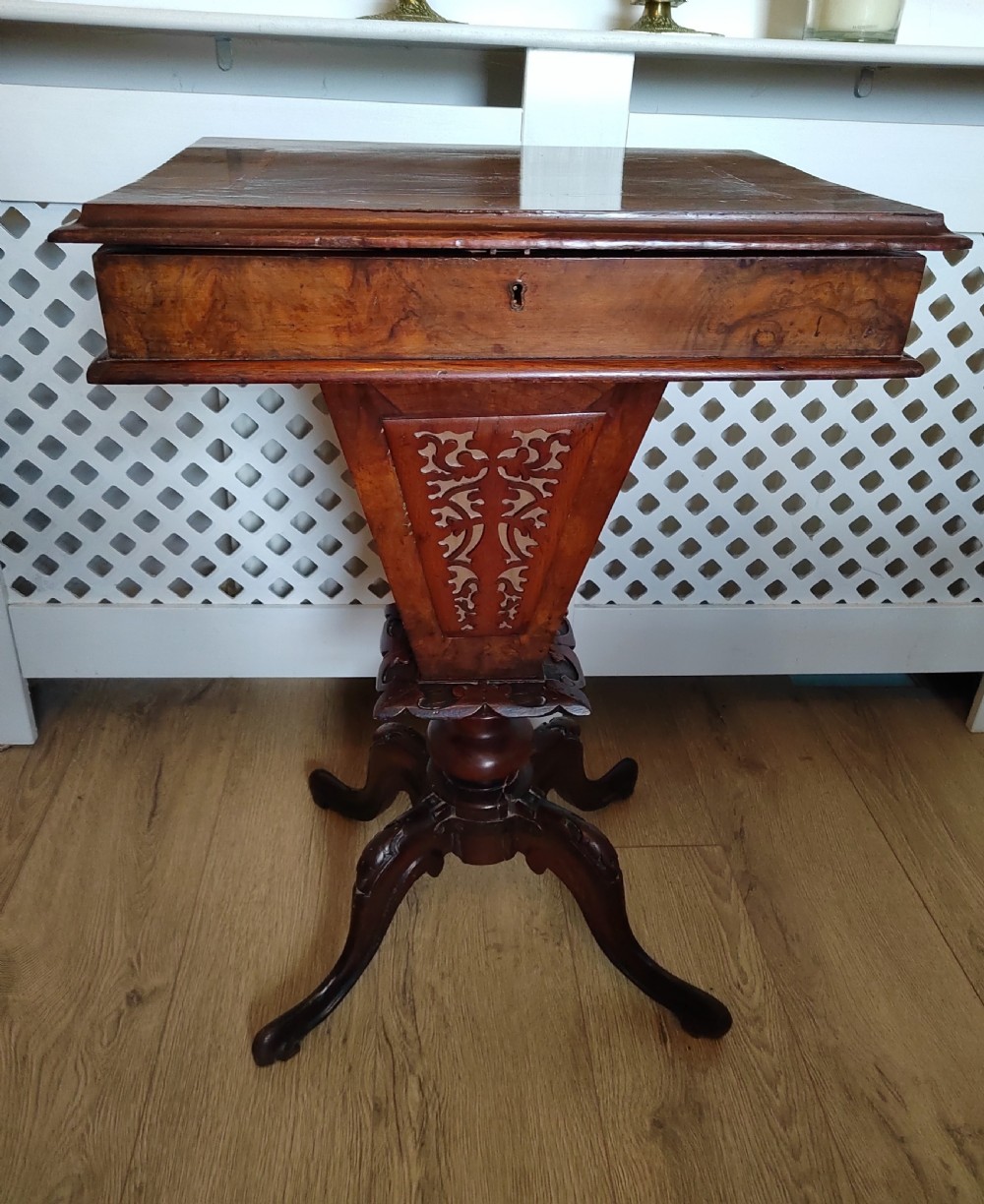 A Victorian wooden trumpet sewing table with an inlaid top, fretwork column, and carved tripod base. View V