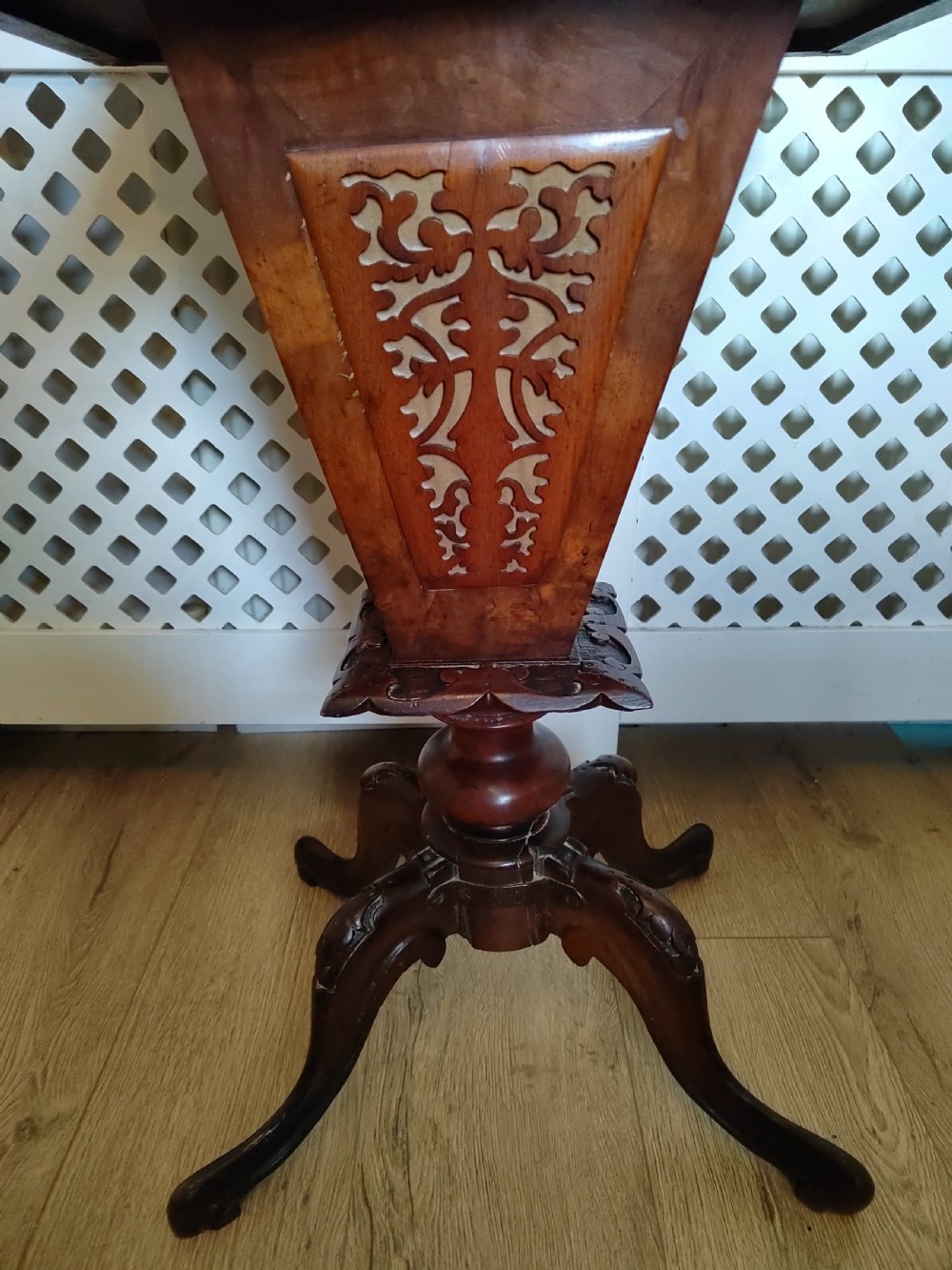 A Victorian wooden trumpet sewing table with an inlaid top, fretwork column, and carved tripod base. View VII