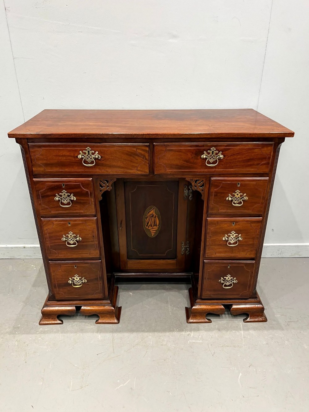 A George III mahogany kneehole desk with multiple drawers, a recessed central inlaid door, brass handles, and bracket feet.