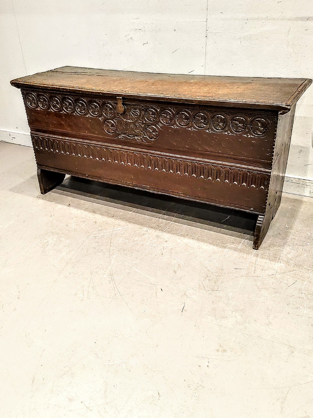 A dark brown 17th-century carved oak coffer with a flat lid, carved roundel frieze, arcaded lower section, and V-cut slab end legs.