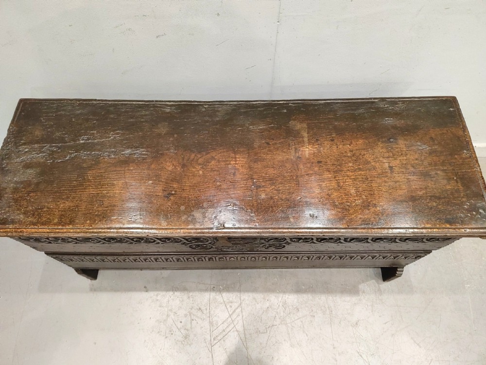 A dark brown 17th-century carved oak coffer with a flat lid, carved roundel frieze, arcaded lower section, and V-cut slab end legs. View II