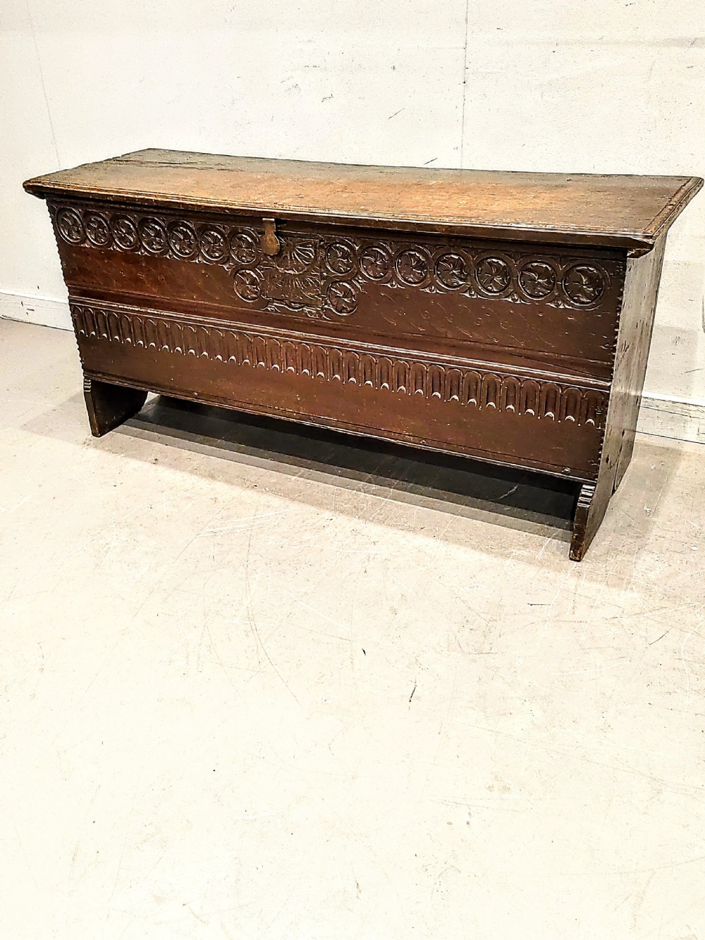 A dark brown 17th-century carved oak coffer with a flat lid, carved roundel frieze, arcaded lower section, and V-cut slab end legs. View IV
